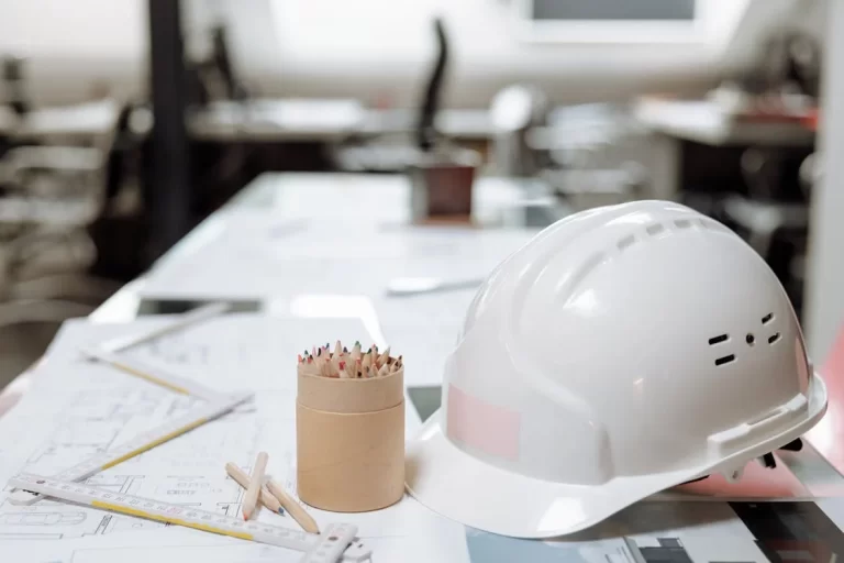 engineering concept image - hard hat and pencils sitting on desk with blueprints and ruler