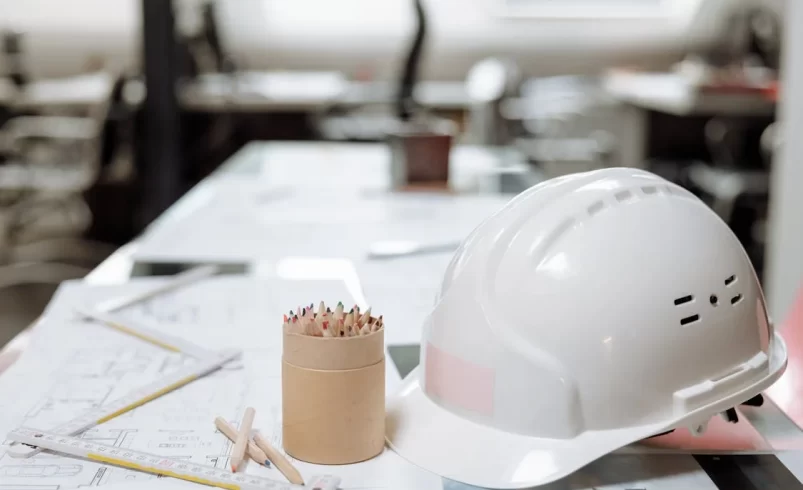 engineering concept image - hard hat and pencils sitting on desk with blueprints and ruler